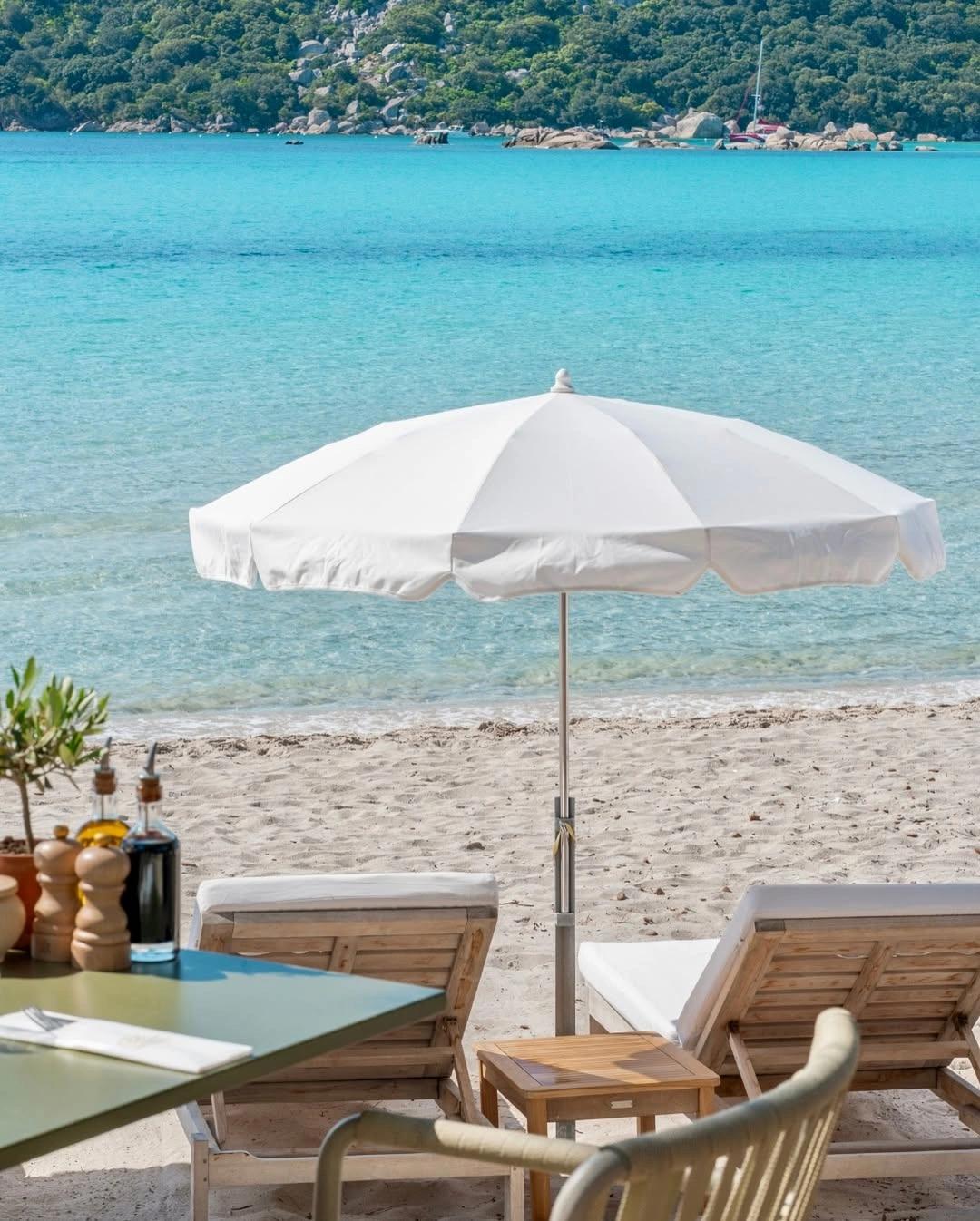 Restaurant de plage à Santa Giulia avec parasol blanc et chaises longues face à la mer turquoise