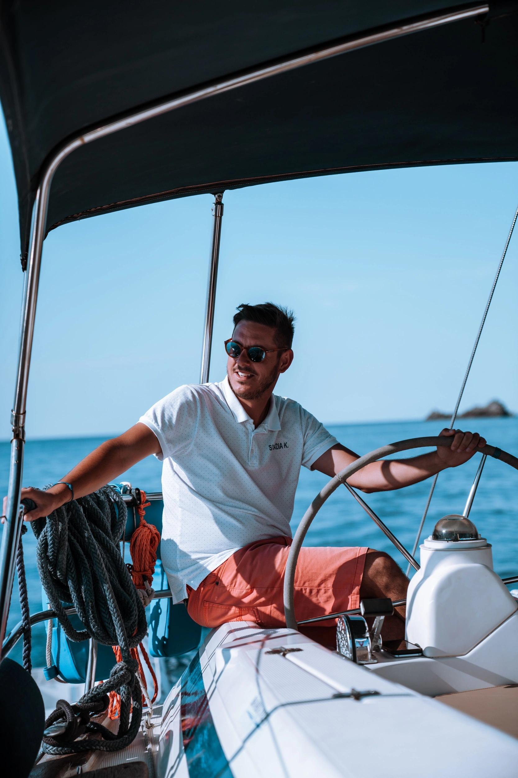 Homme souriant à la barre d'un voilier lors d'une location de bateau à Santa Giulia
