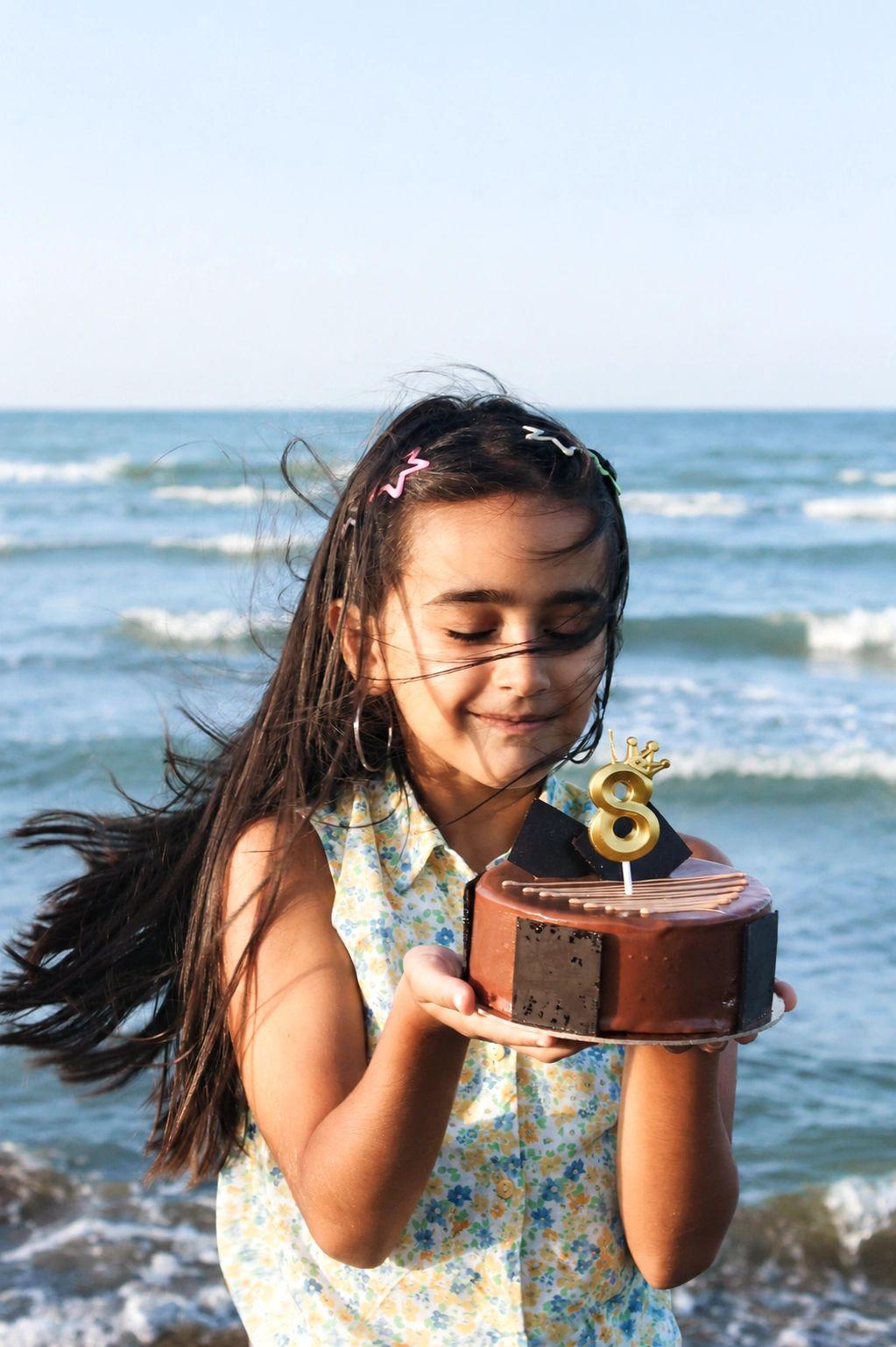 Jeune fille tenant un gâteau d'anniversaire à la plage de Santa Giulia pour événements privés et mariages