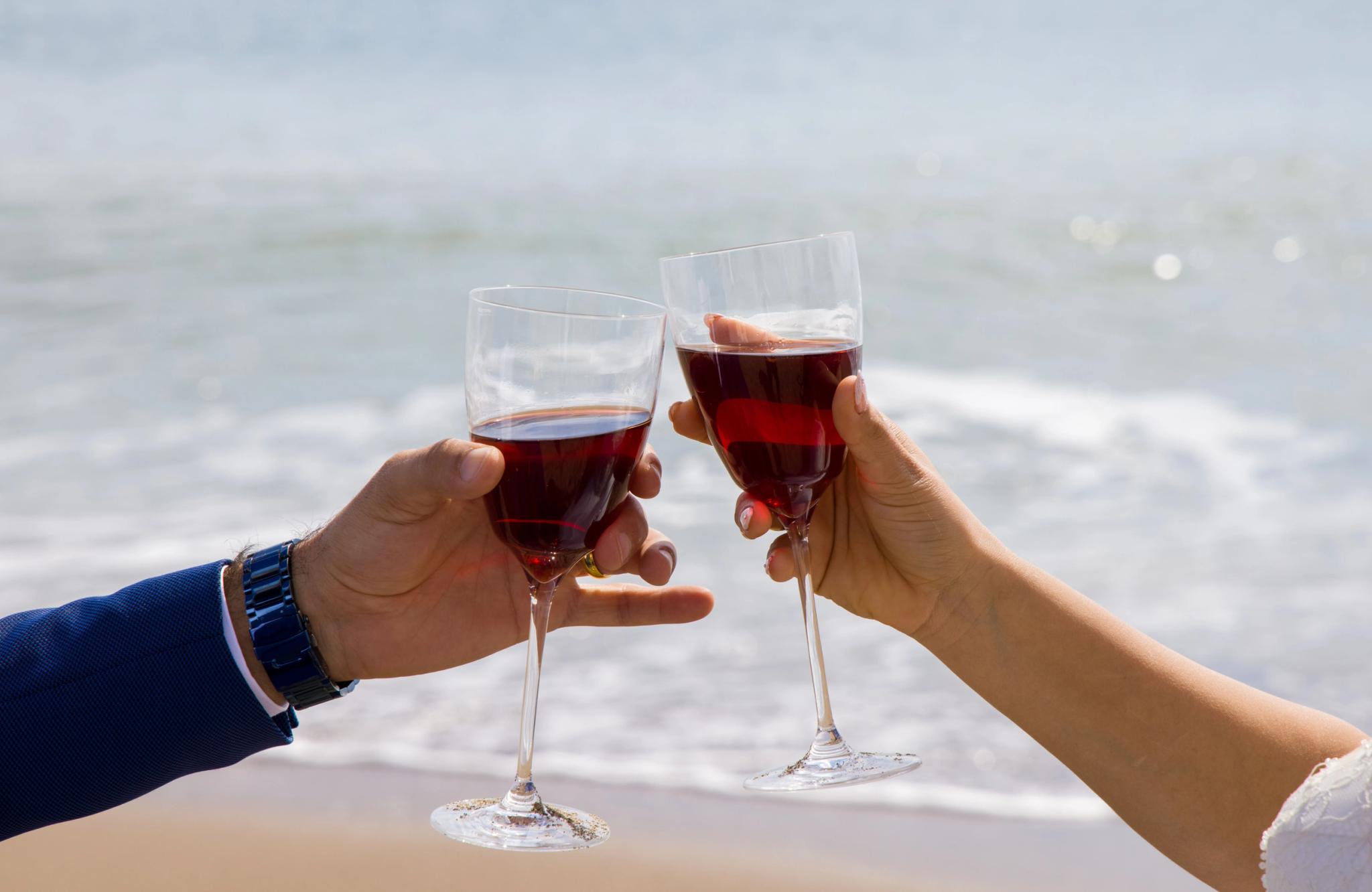 Deux personnes trinquent avec des verres de vin rouge sur la plage de Santa Giulia